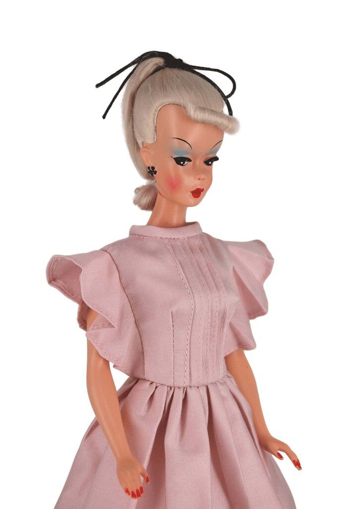 Bild Lilli doll in a blush pink dress with pintuck details, ruffled sleeves, and a pleated skirt, capturing classic mid-century charm.