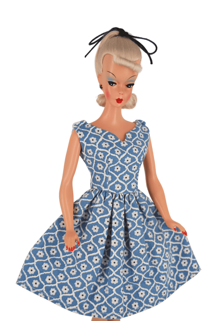 Bild Lilli doll in a blue floral dress with an asymmetrical neckline and pleated skirt, capturing mid-century charm and timeless style.