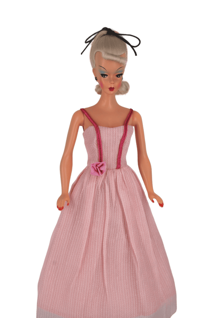 Bild Lilli doll in a blush pink ball gown with delicate straps, a fabric rose at the waist, and a pleated full skirt, evoking vintage glamour.