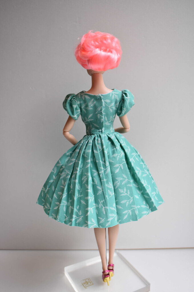 Handmade mint green doll dress with delicate white botanical details, puffed sleeves, fitted waist, and a flowing pleated skirt. Timeless vintage charm.