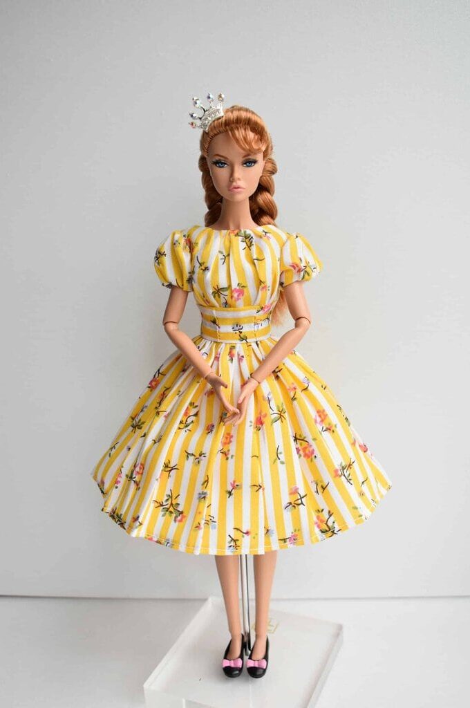 Bright yellow doll dress featuring white stripes, puffed sleeves, a structured bodice, and pleated skirt with a delicate floral pattern. Classic vintage style.