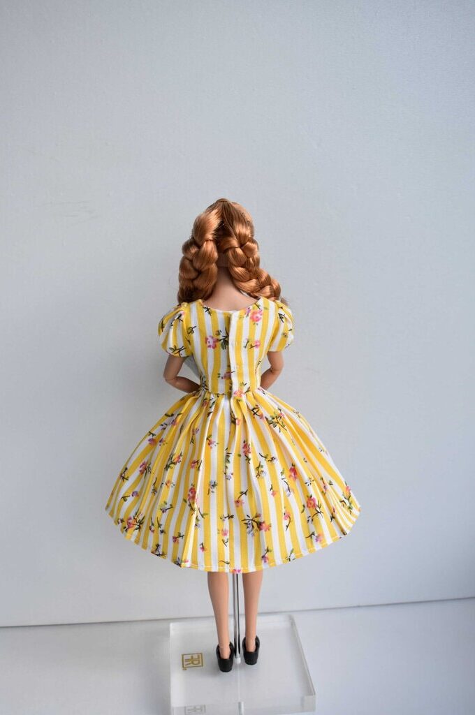 Handmade yellow and white striped doll dress with delicate floral details, puffed sleeves, fitted waist, and a flowing pleated skirt. Timeless retro charm.