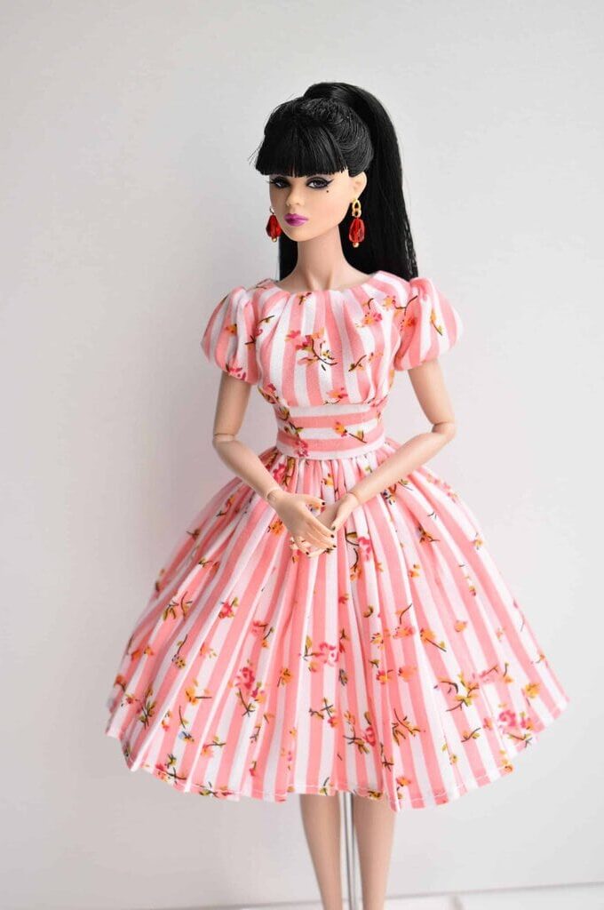 Elegant pink doll dress featuring white stripes, puffed sleeves, a structured bodice, and a pleated skirt with a delicate floral pattern. Classic vintage style.