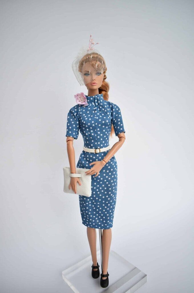 Elegant blue polka dot doll dress featuring a fitted silhouette, high neckline, and pleated bodice. Retro chic with a refined touch.