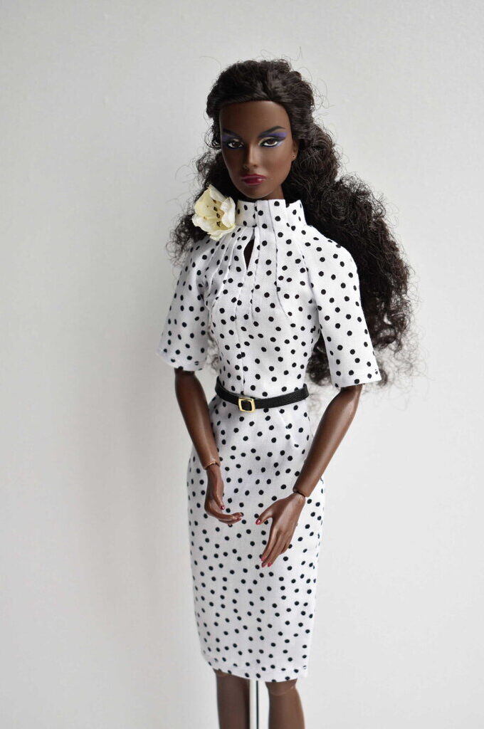 Elegant white polka dot doll dress featuring a fitted silhouette, high neckline, and pleated bodice. Retro chic with a refined touch.