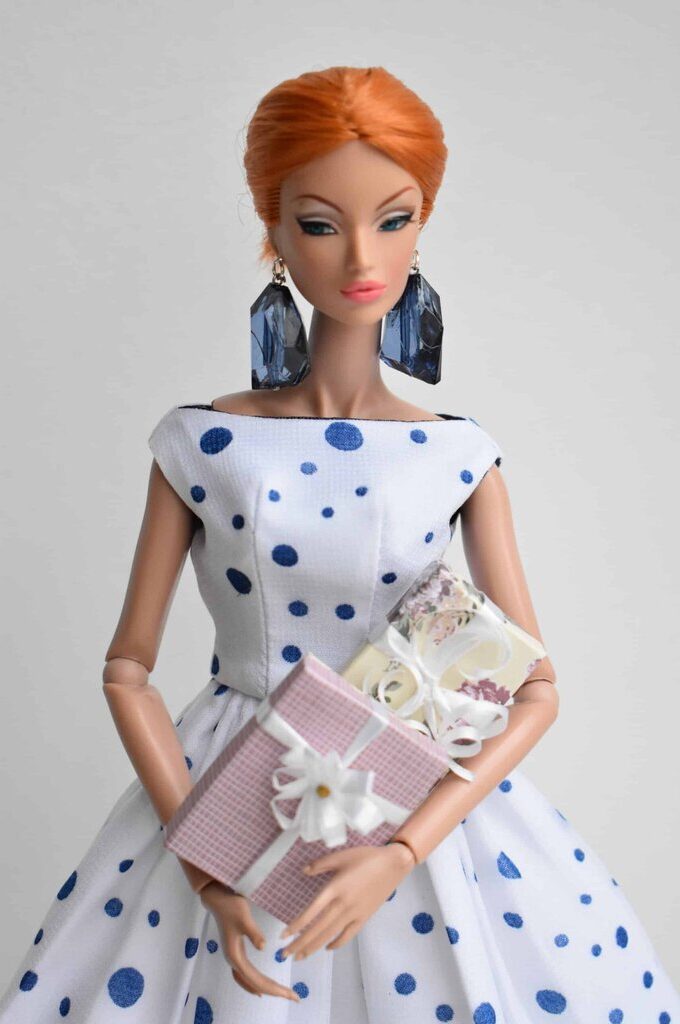 White fit-and-flare dress with scattered blue polka dots, a bateau neckline, and a voluminous pleated skirt, capturing vintage elegance with a playful twist.