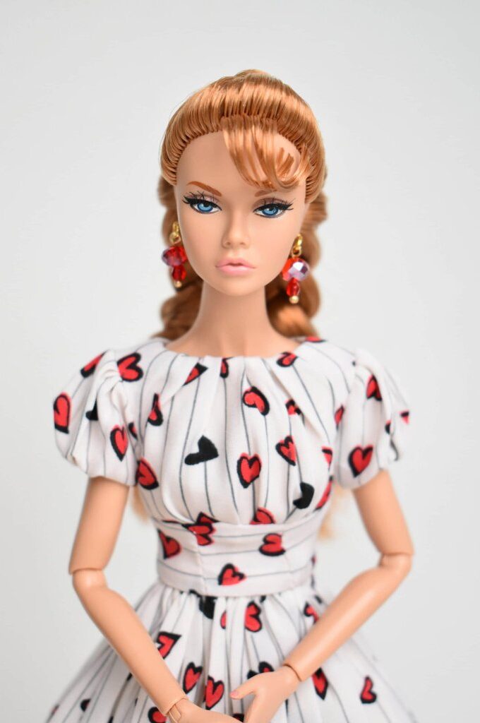 A retro-inspired doll dress featuring a white fabric with red and black heart prints, delicate pinstripes, puff sleeves, a fitted waist, and a full pleated skirt for a timeless vintage look.