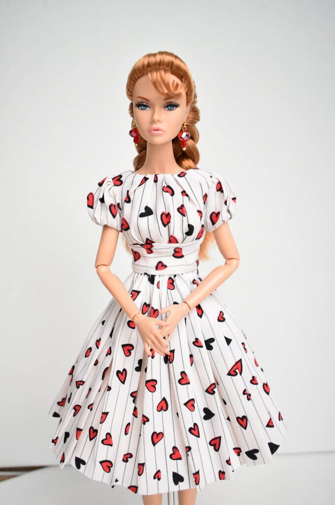 Elegant doll dress with a heart-patterned design, puffed short sleeves, pleated full skirt, and tailored waist, evoking a classic 1950s aesthetic with a modern playful twist.