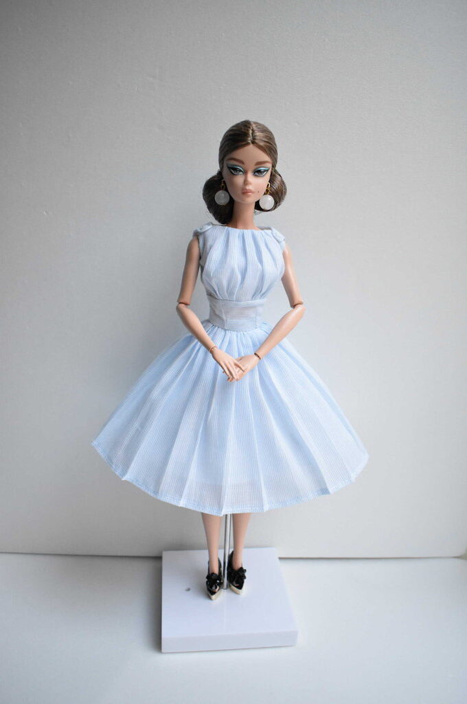 Classic light blue striped doll dress with cap sleeves, a structured waist, and a flowing pleated skirt, designed to evoke timeless elegance with a soft, feminine silhouette.