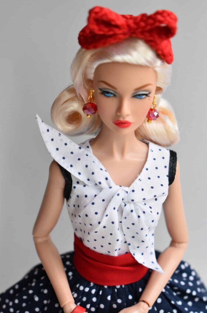 Vintage-inspired navy polka dot doll dress with a sleeveless blouse, lace-trimmed accents, and a dramatic full skirt, capturing the essence of mid-century fashion with a bold red waist tie.