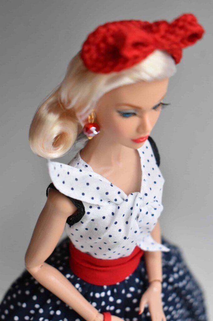 Retro polka dot doll dress with a white sleeveless blouse, statement bow, black lace accents, and a full navy skirt with white polka dots, finished with a bold red waistband for a classic vintage appeal.