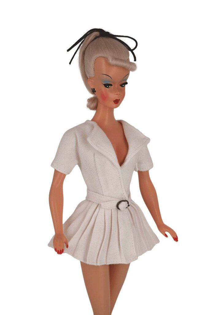 Bild Lilli doll in a white pleated jacket dress with a cinched waist and belt, showcasing tailored elegance and vintage-inspired style.